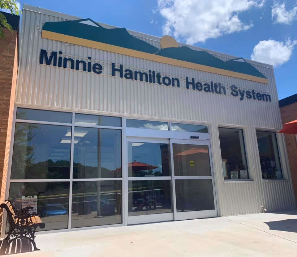 Front view of Minnie Hamilton Health System building with glass entrance and blue sky.