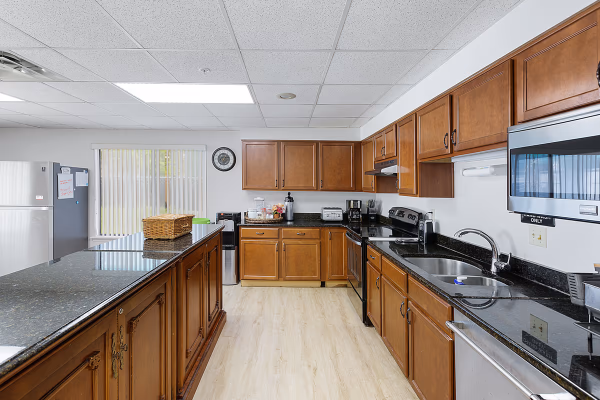 Communal kitchen with wooden cabinets, black granite countertops, a center island, and stainless appliances.