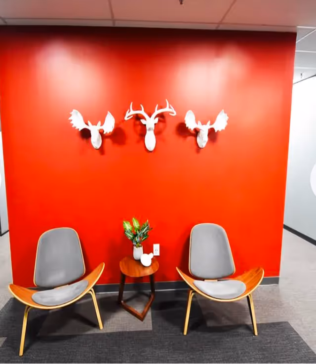 Red wall seating area with two modern chairs, a small round table, and plant decor.