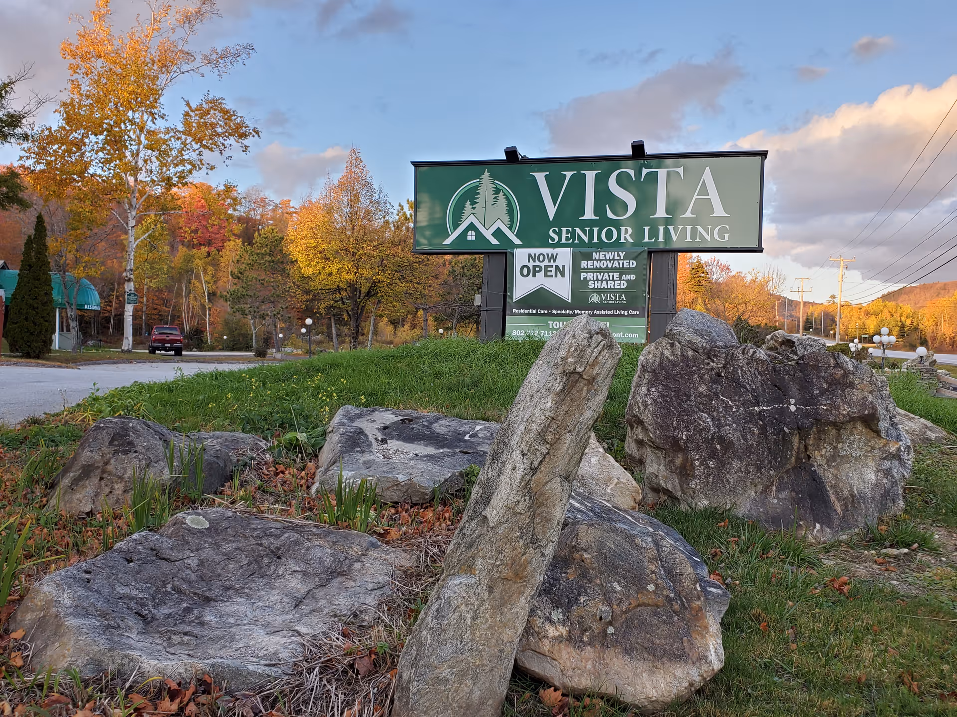 Outdoor view of Vista Senior Living sign surrounded by rocks and autumn trees.