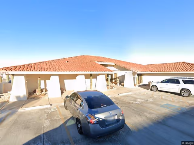 Exterior of a single-story facility with a red-tiled roof and parked cars.