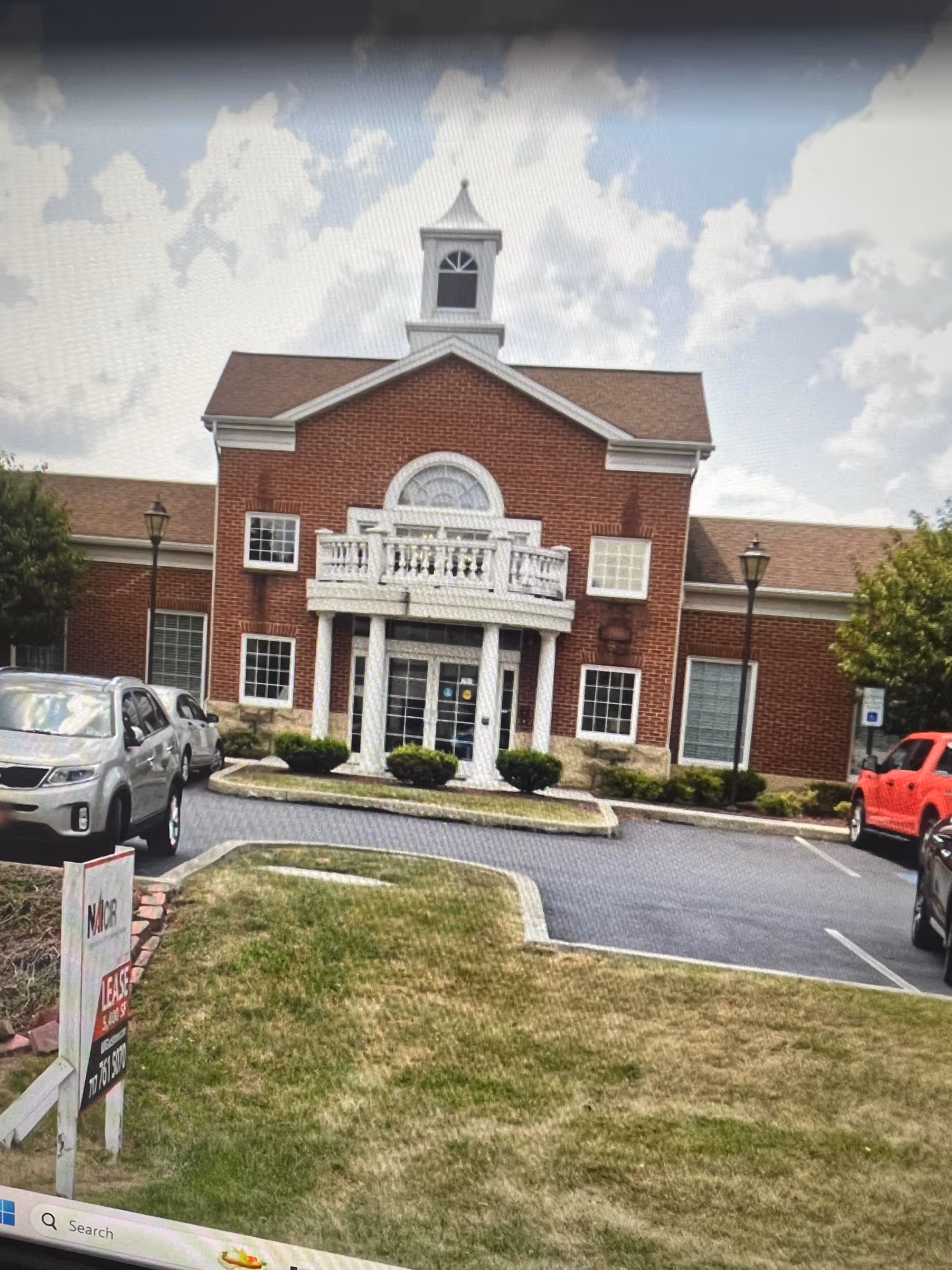 Brick building with a white entrance and a parking lot outside.