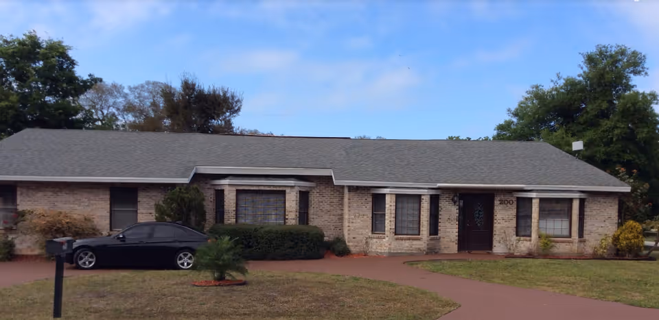 Brick exterior of La Poinciana ALF with driveway, bushes, and a parked car.