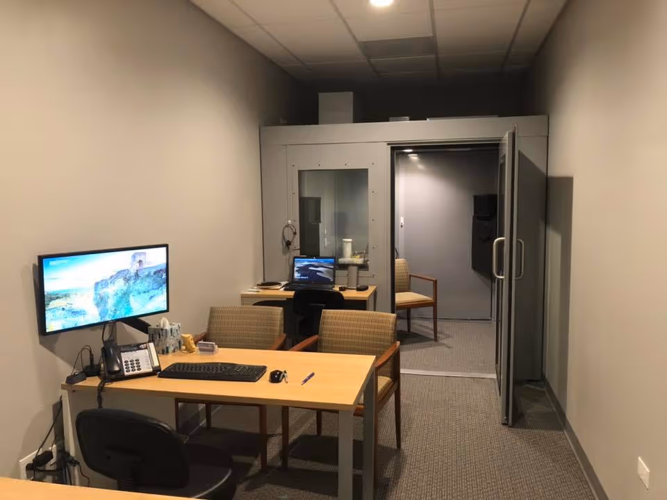 A small office with desks, computers, and chairs inside a facility.