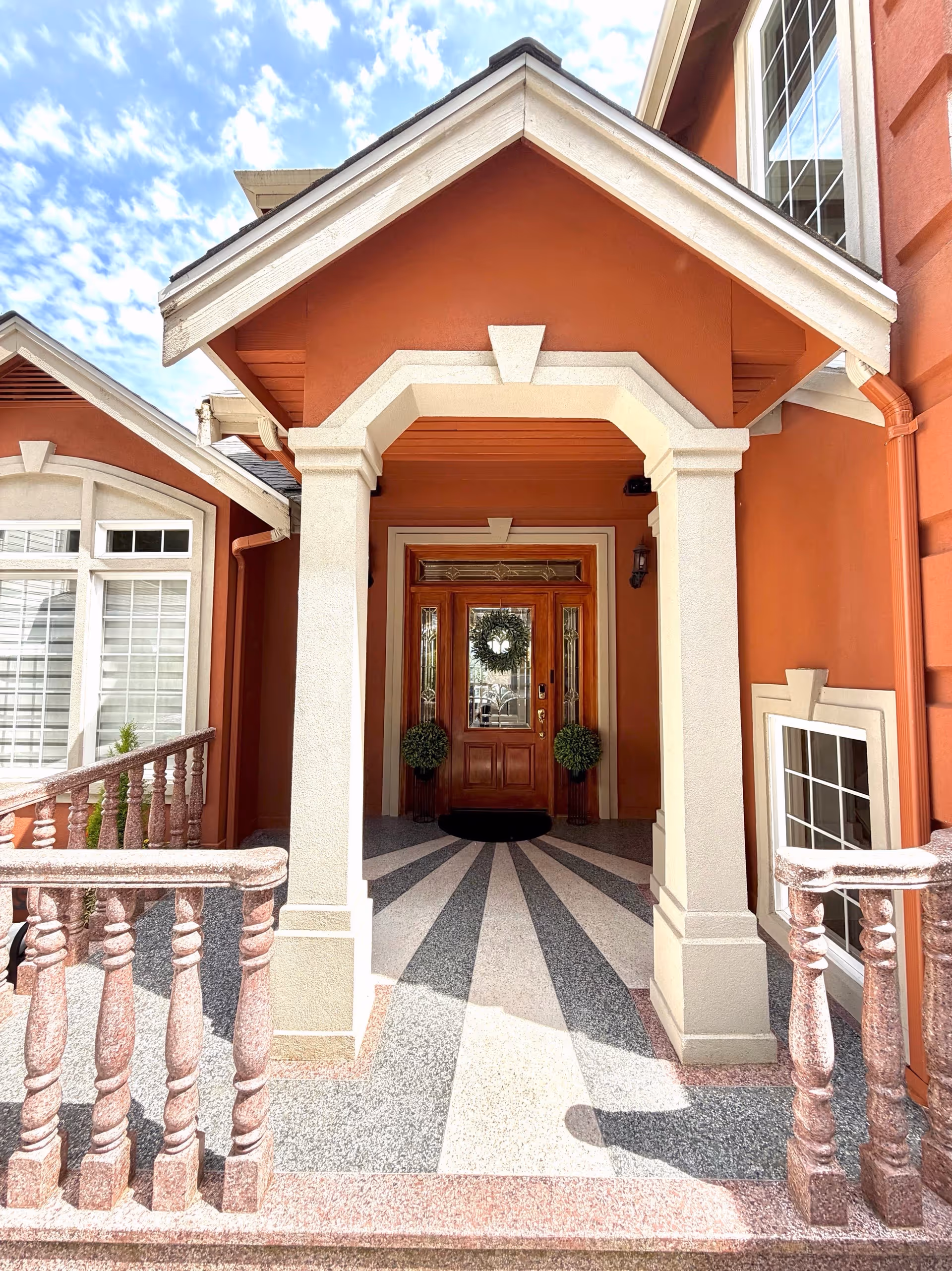 Orange building entrance with white columns, arched entry, and decorative patterned tile walkway.