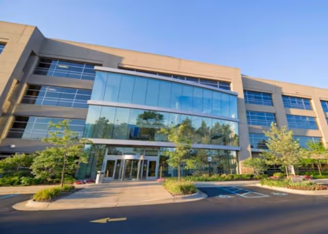 Modern multi-story building with glass entrance and landscaped surroundings.
