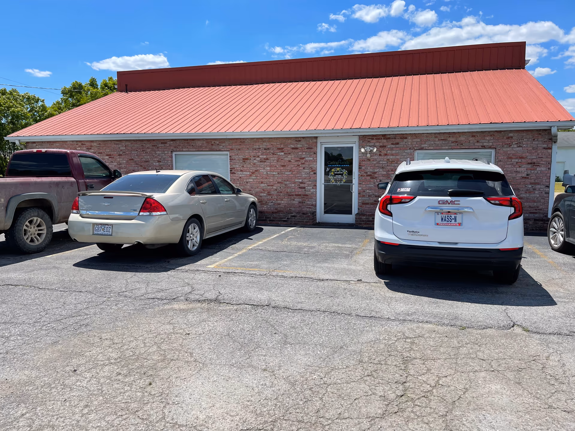 Brick building with a red metal roof and several cars parked in front.