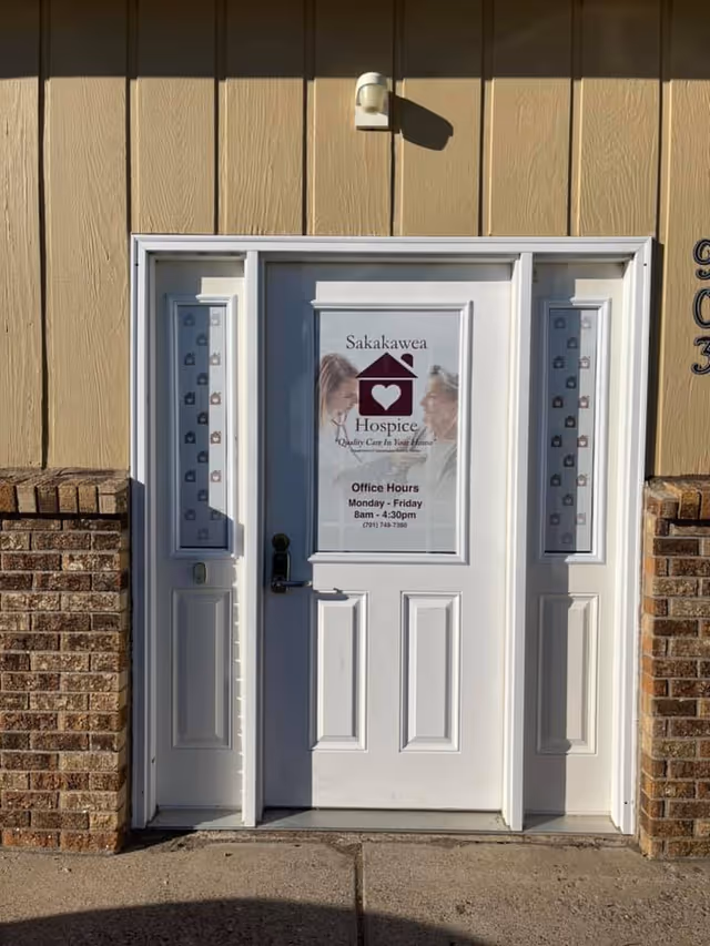 White exterior entry door featuring Sakakawea Hospice sign and office hours.