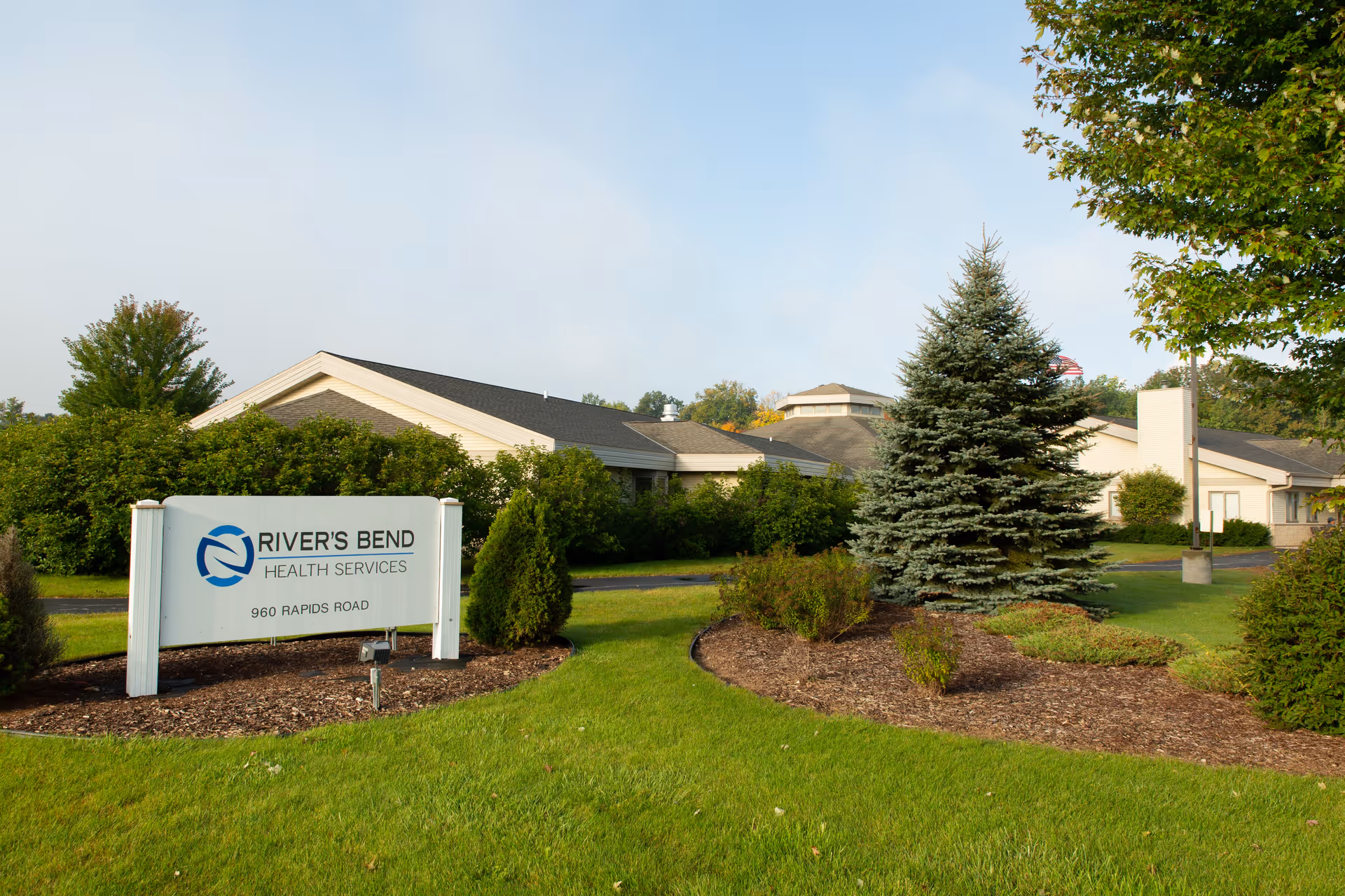 Landscaped lawn and entrance sign in front of the River's Bend Health Services building with trees and shrubs.