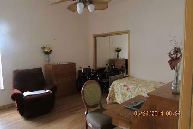 A furnished bedroom in Summerhaven Assisted Living with bed, dresser, desk, and chair.