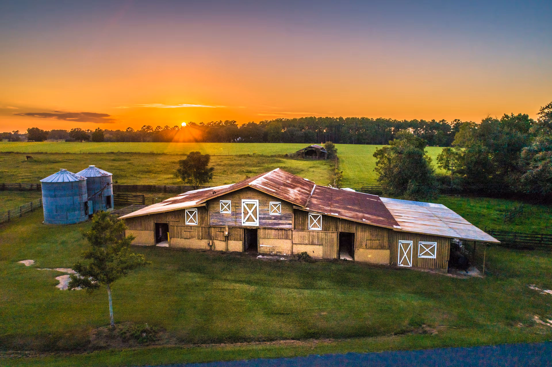 Sunset over a weathered barn, silos, and green pastures.