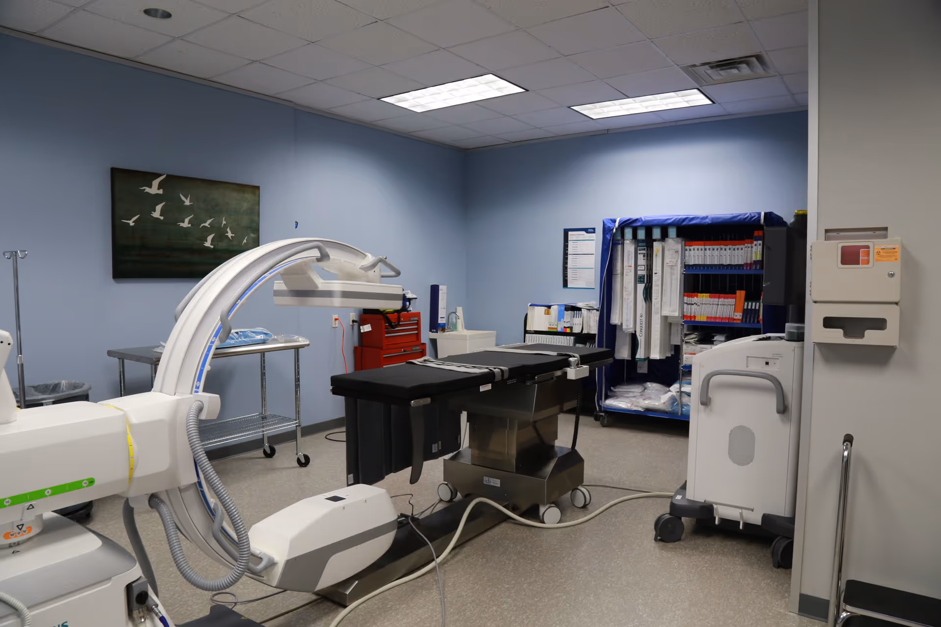 Medical procedure room featuring a surgical table, C-arm imaging system, and organized medical equipment.