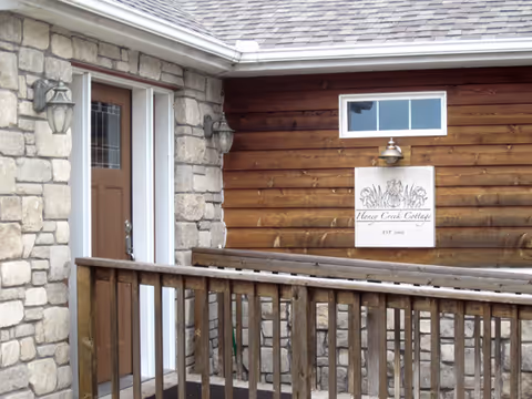 Stone and wood exterior of Honey Creek Cottage with a front door and sign.