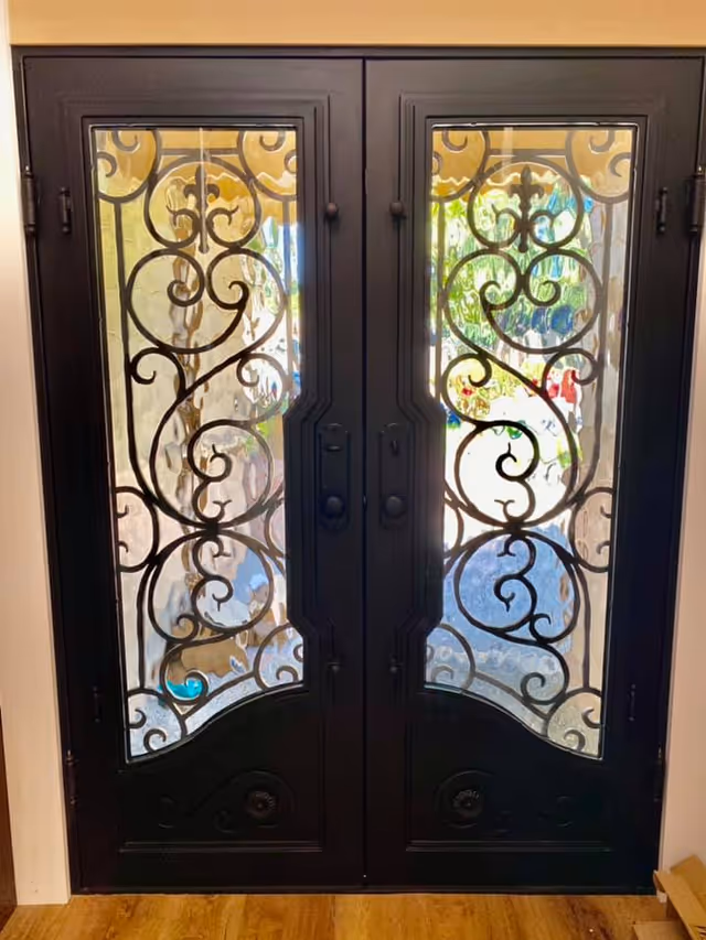 Black double doors with intricate wrought-iron glass panels in a residential entryway.