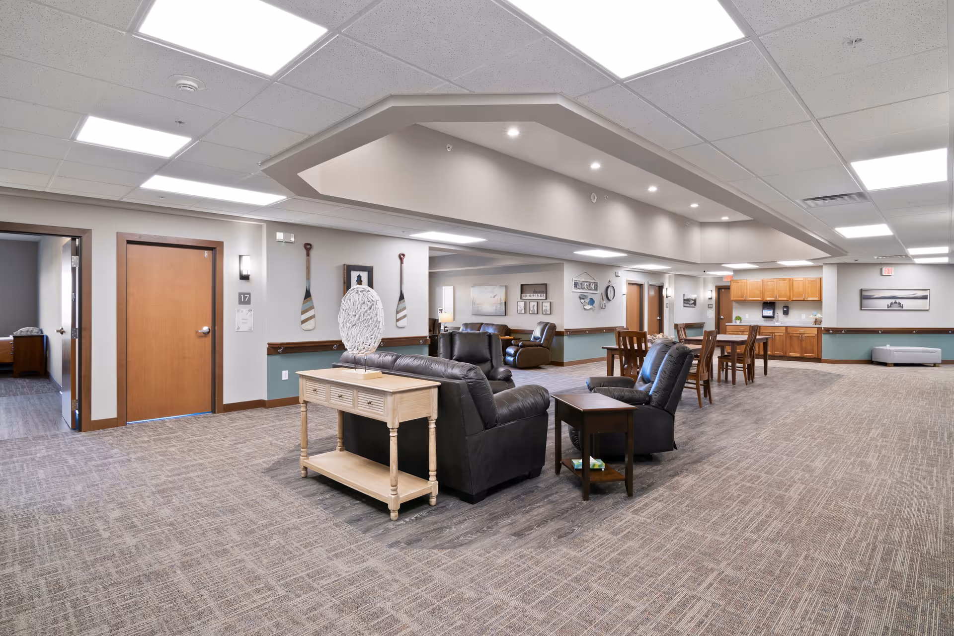 Open, spacious senior living common area with couches, chairs, tables, and a kitchenette along the back.