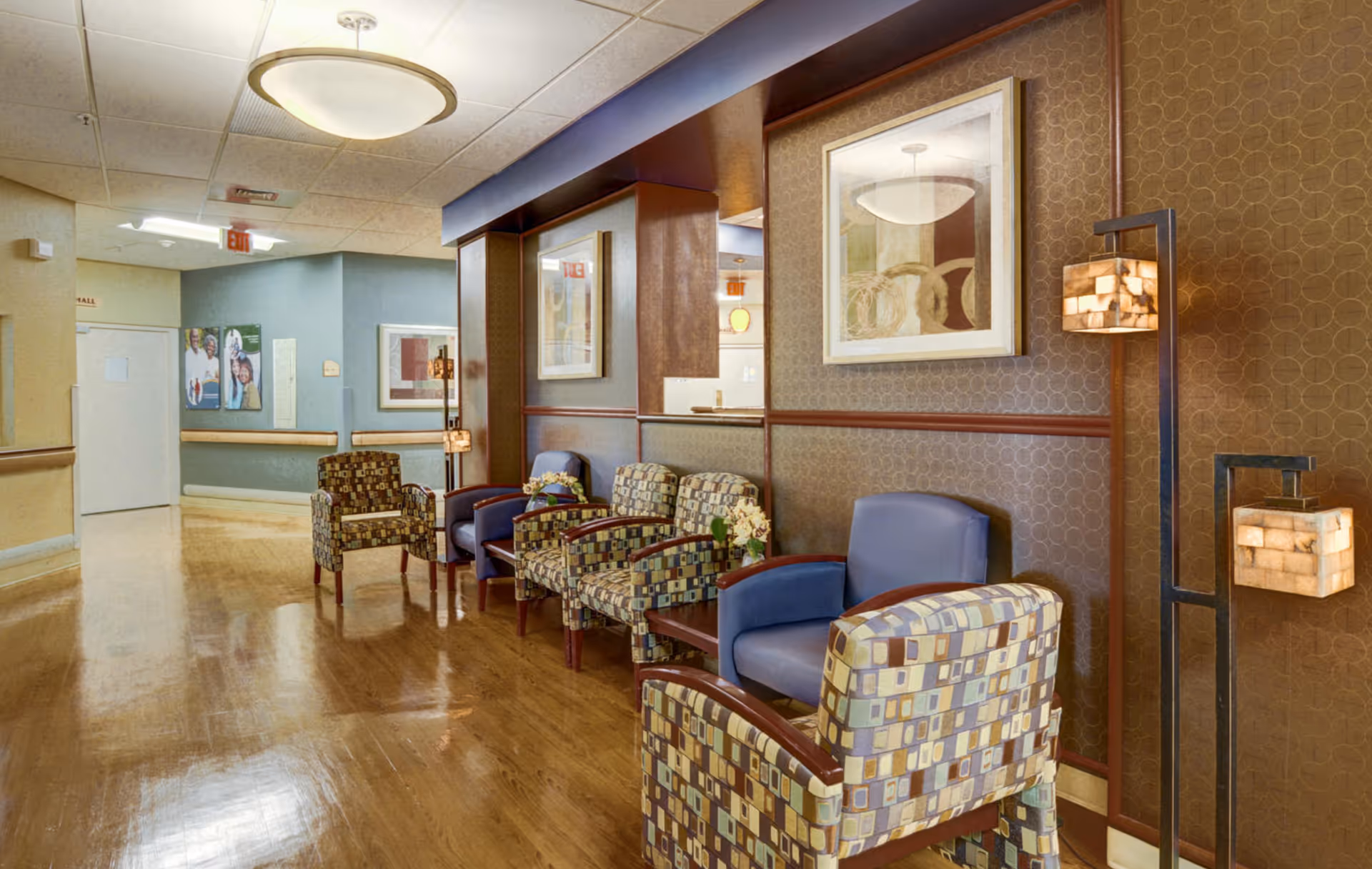 Warm lobby seating area with patterned chairs, lamps, and framed art along wood floors.