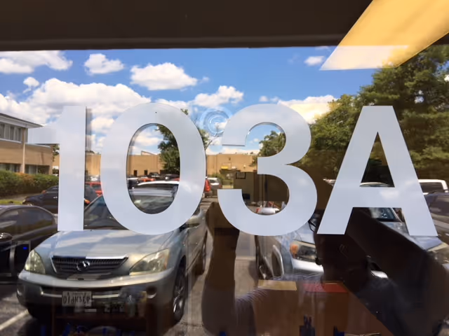 Storefront glass shows the number 103A with reflections of parked cars.
