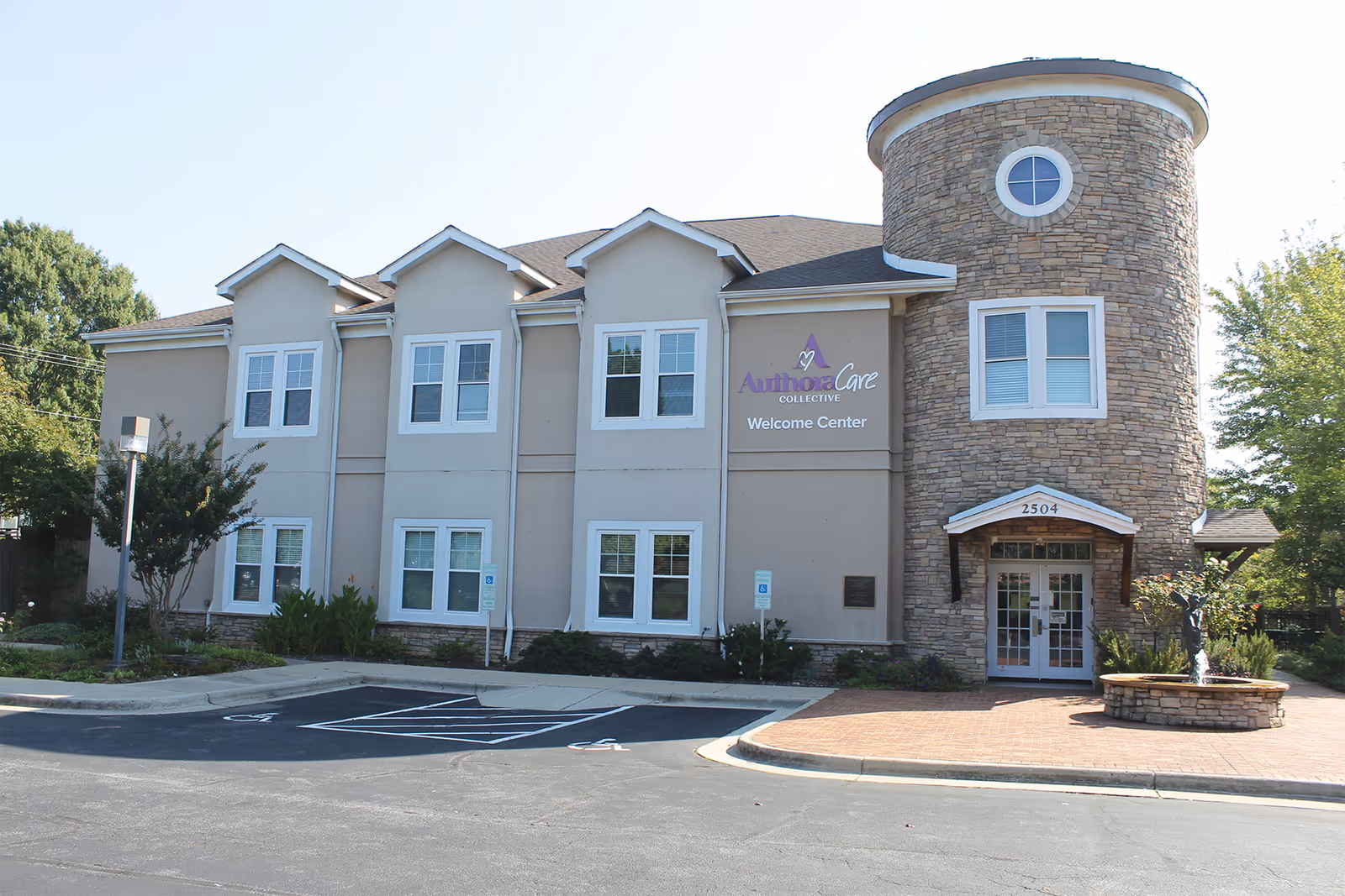 Exterior view of AuthoraCare Collective Greensboro Welcome Center building with stone tower and parking lot.