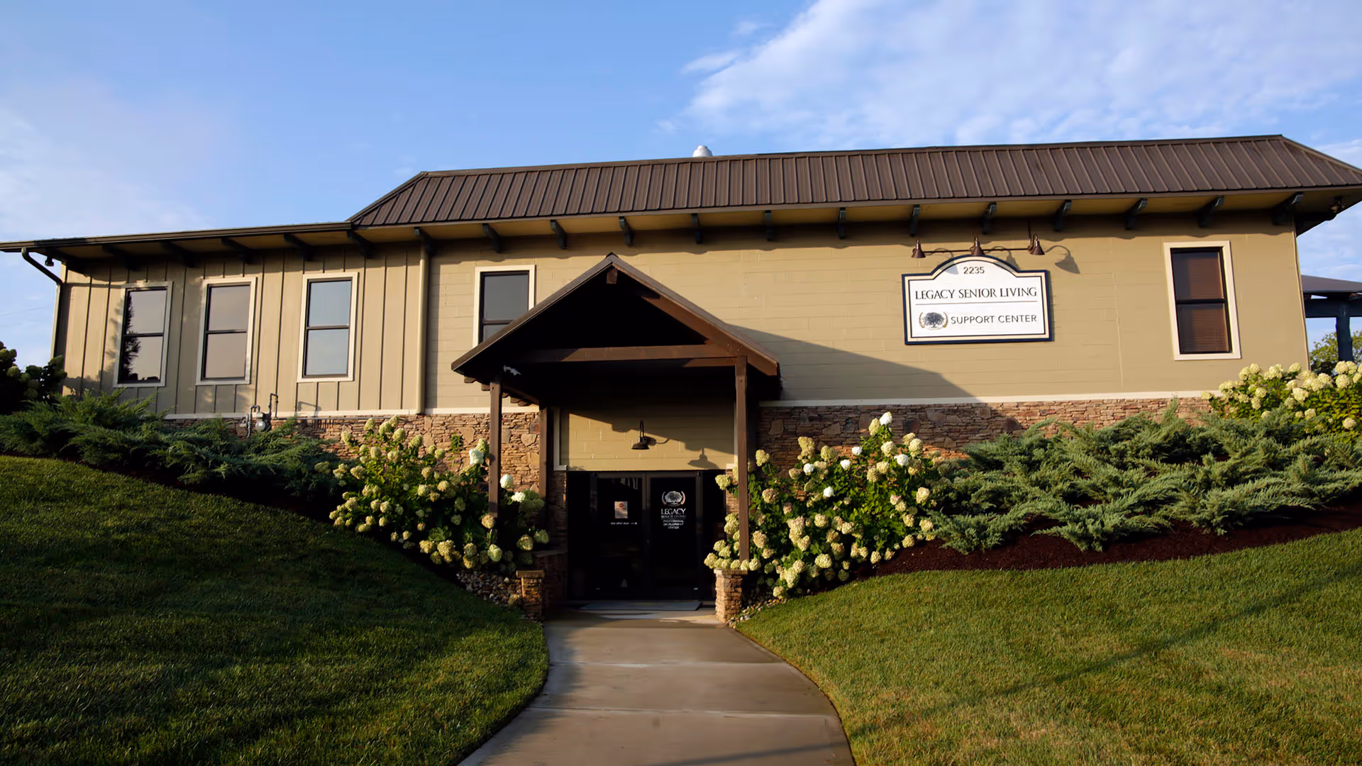 Front exterior of Legacy Senior Living Support Center with landscaped bushes and a walkway.