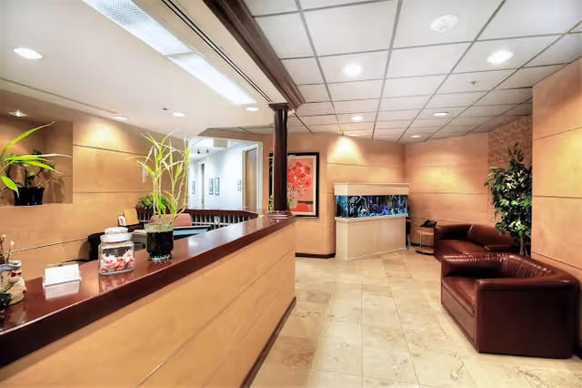 Bright senior living lobby with a long wooden reception desk, plants, seating, and a fish tank.
