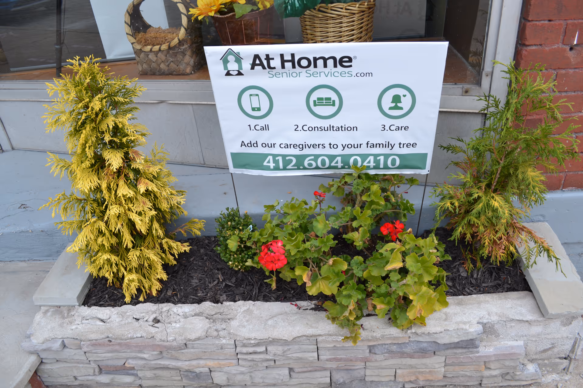 Exterior storefront with an At Home Senior Services sign and potted plants in a planter.