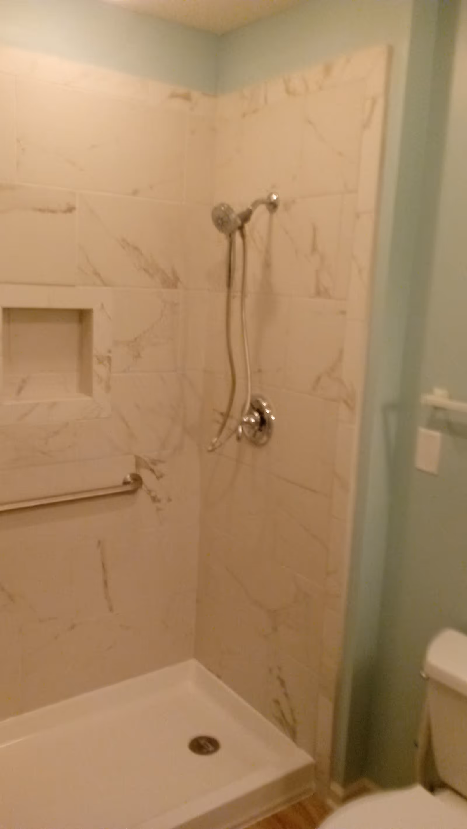 A tiled walk-in shower with handheld showerhead and grab bar