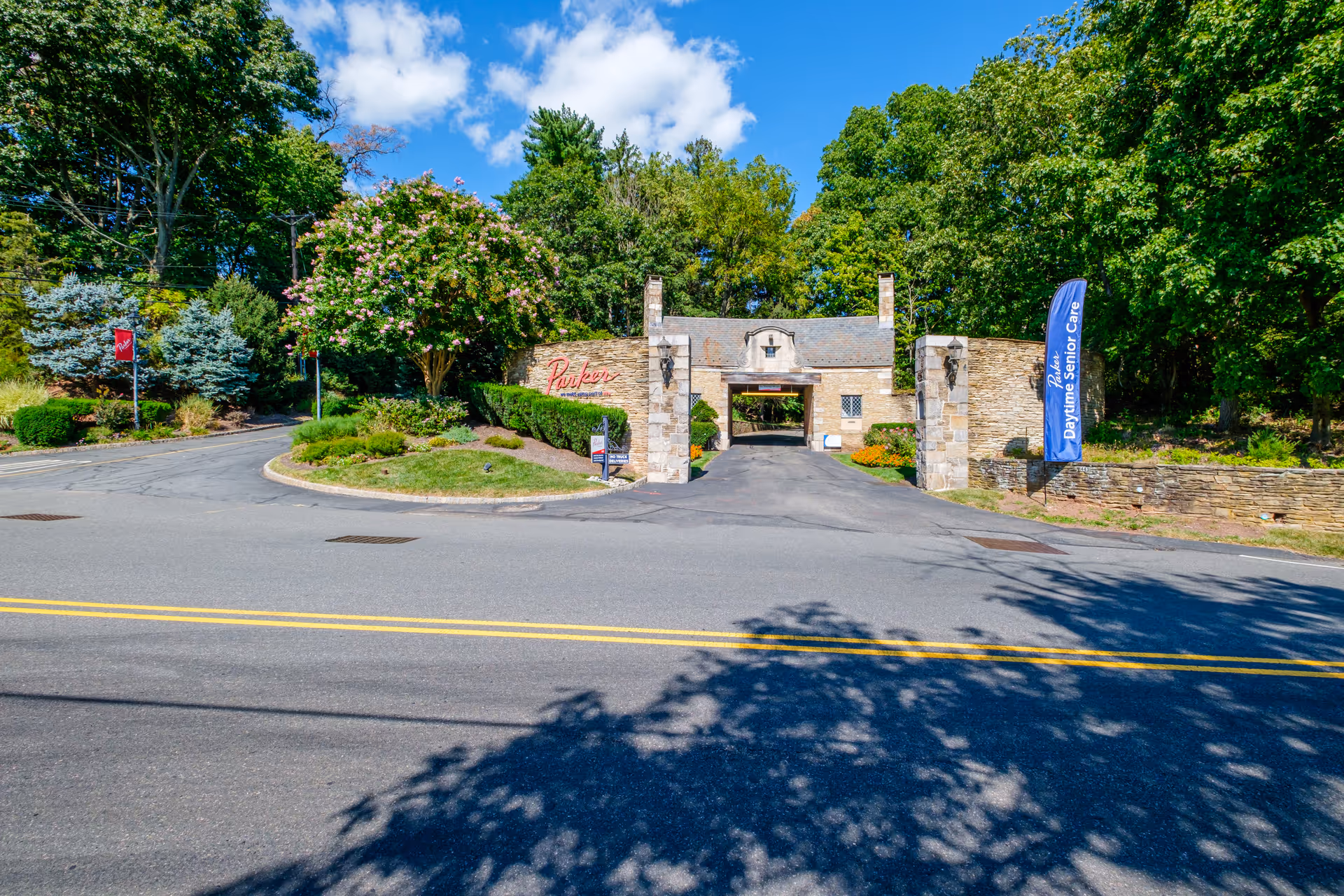Stone entrance gatehouse and drive of the Parker at Stonegate facility with landscaping and trees.