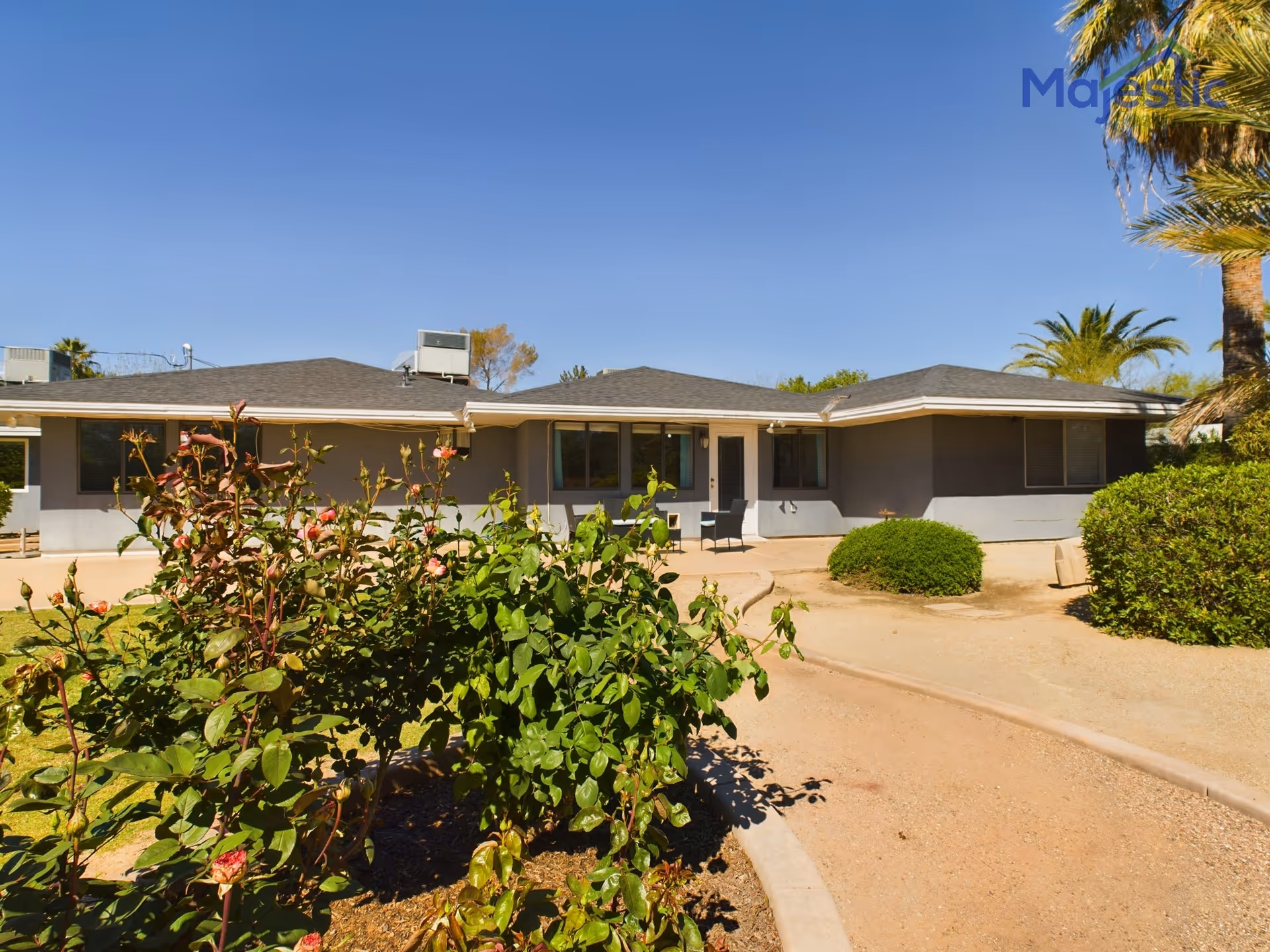 Single-story gray senior living facility with desert landscaping and front patio seating.
