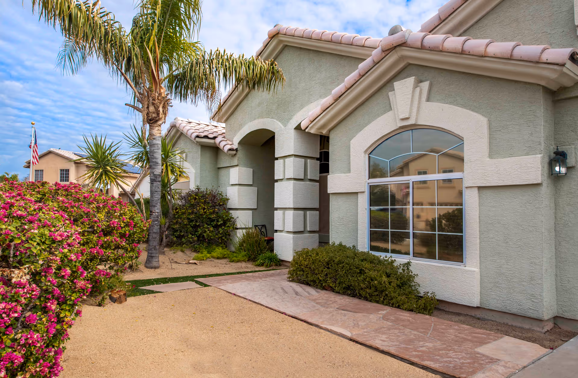 Front exterior of a pale green senior living facility with arched window and palm trees.