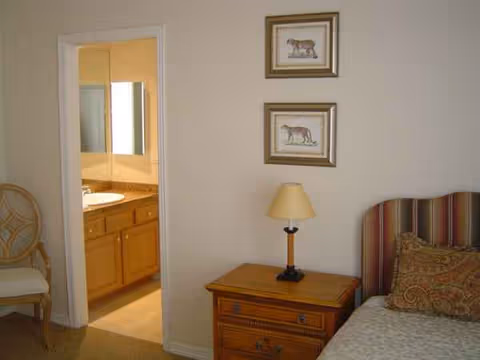 Bedroom with bed, nightstand, lamp, framed horse pictures, and an open bathroom door.