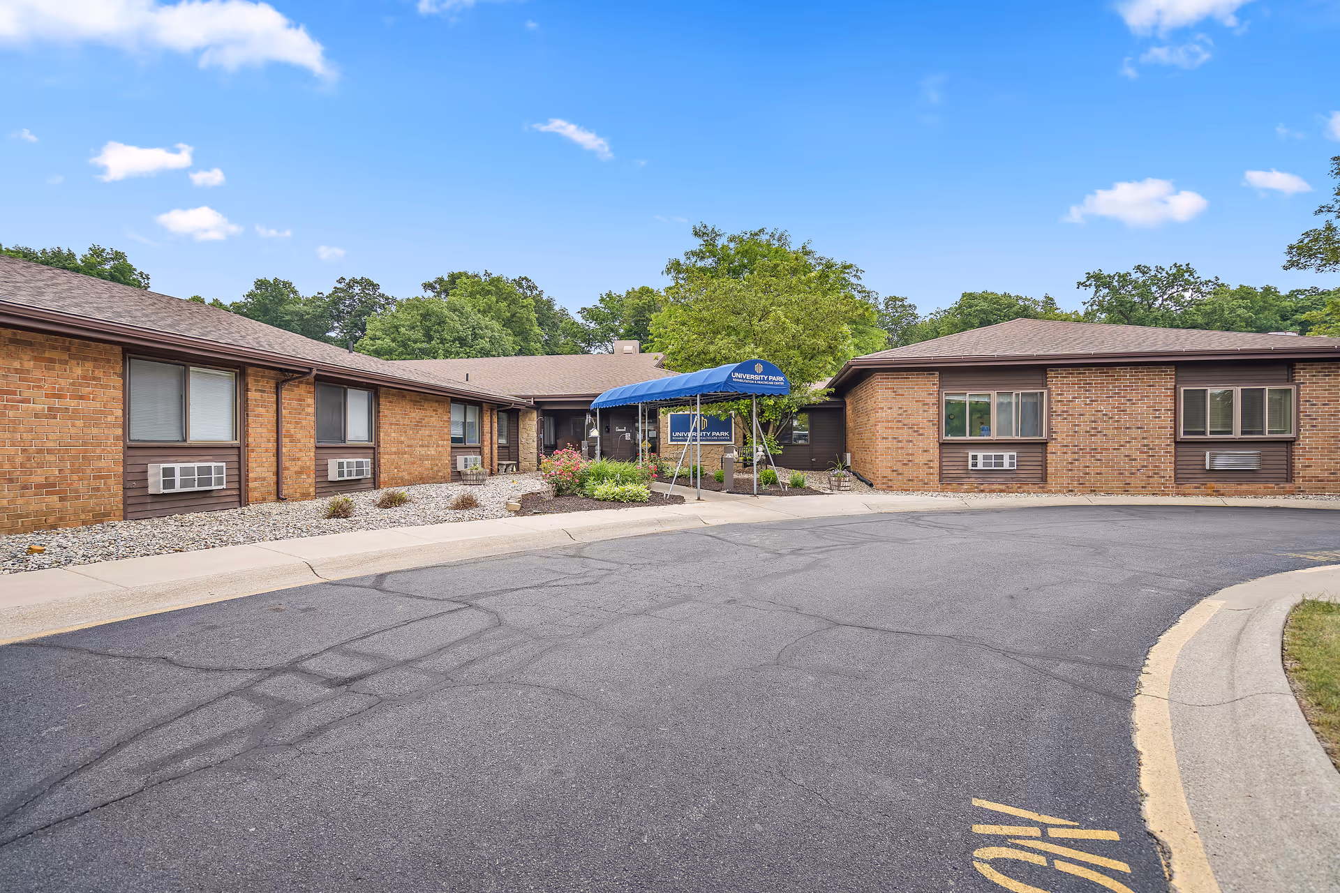 Front view of a single-story brick senior living facility with a blue canopy entrance.