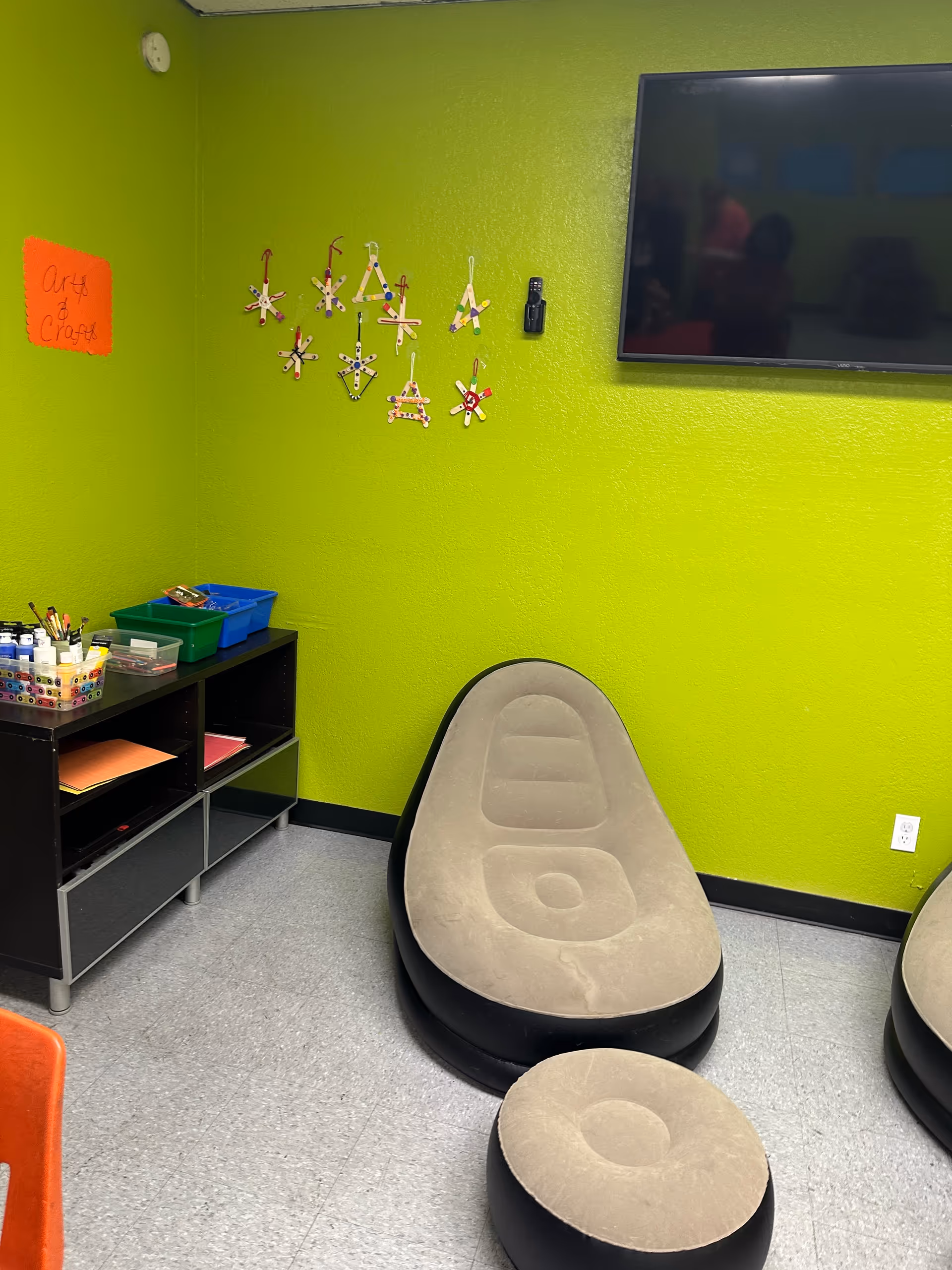 Bright lime green activity room with bean bag seating, TV, and craft supplies.
