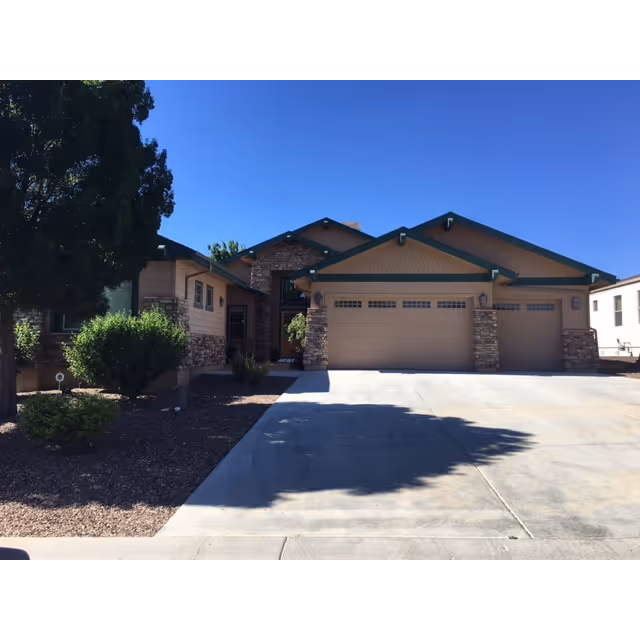 Single-story residential building with a three-car garage, stone accents, front landscaping and a concrete driveway under a clear blue sky.
