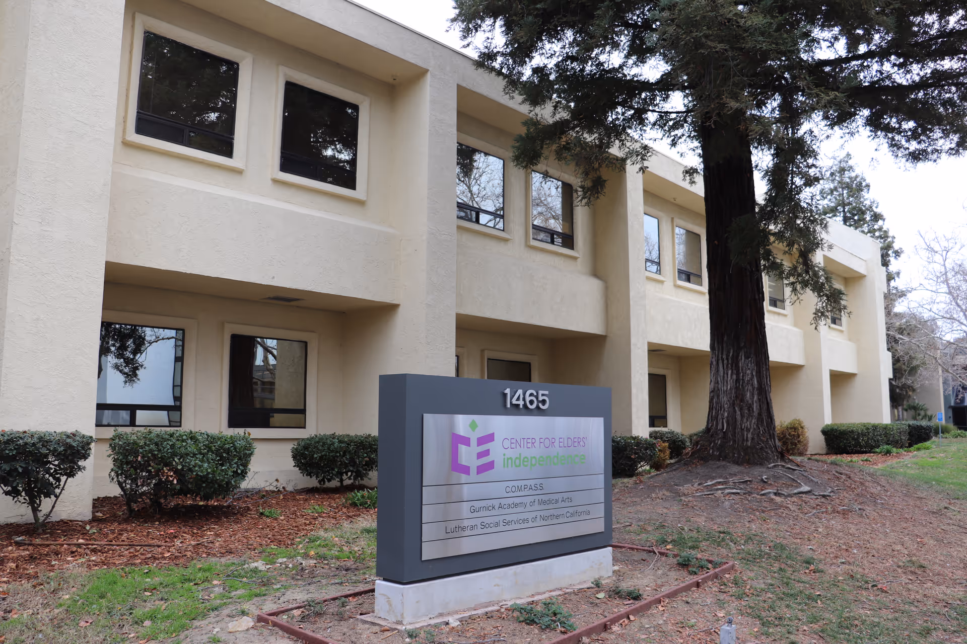 Two-story beige building exterior with a large sign in foreground for Center for Elders' Independence.