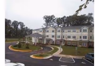 Exterior view of Oaks of Wellington senior living building with entrance, curved driveway, and parking.