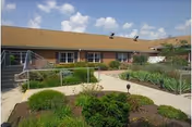 Exterior view of a single-story brick nursing home with landscaped walkway and shrubs