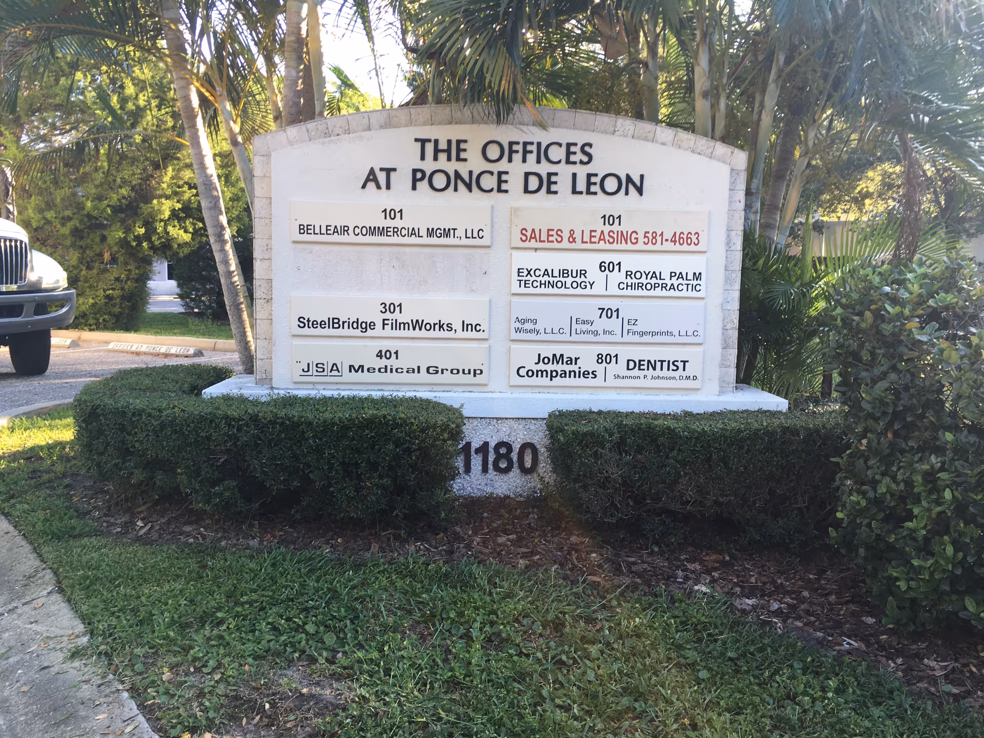 A stone sign reading 'The Offices at Ponce de Leon' with tenant listings and landscaping.