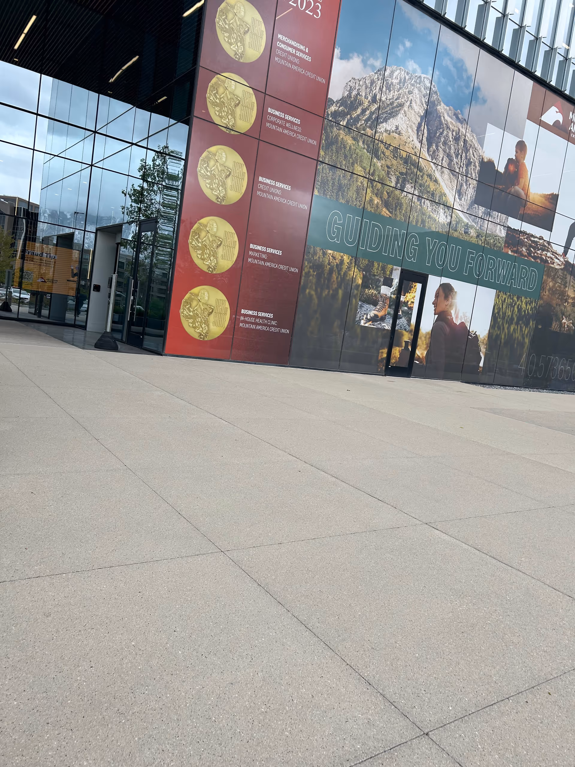 Modern glass building exterior with a large mural featuring mountains along the wall.
