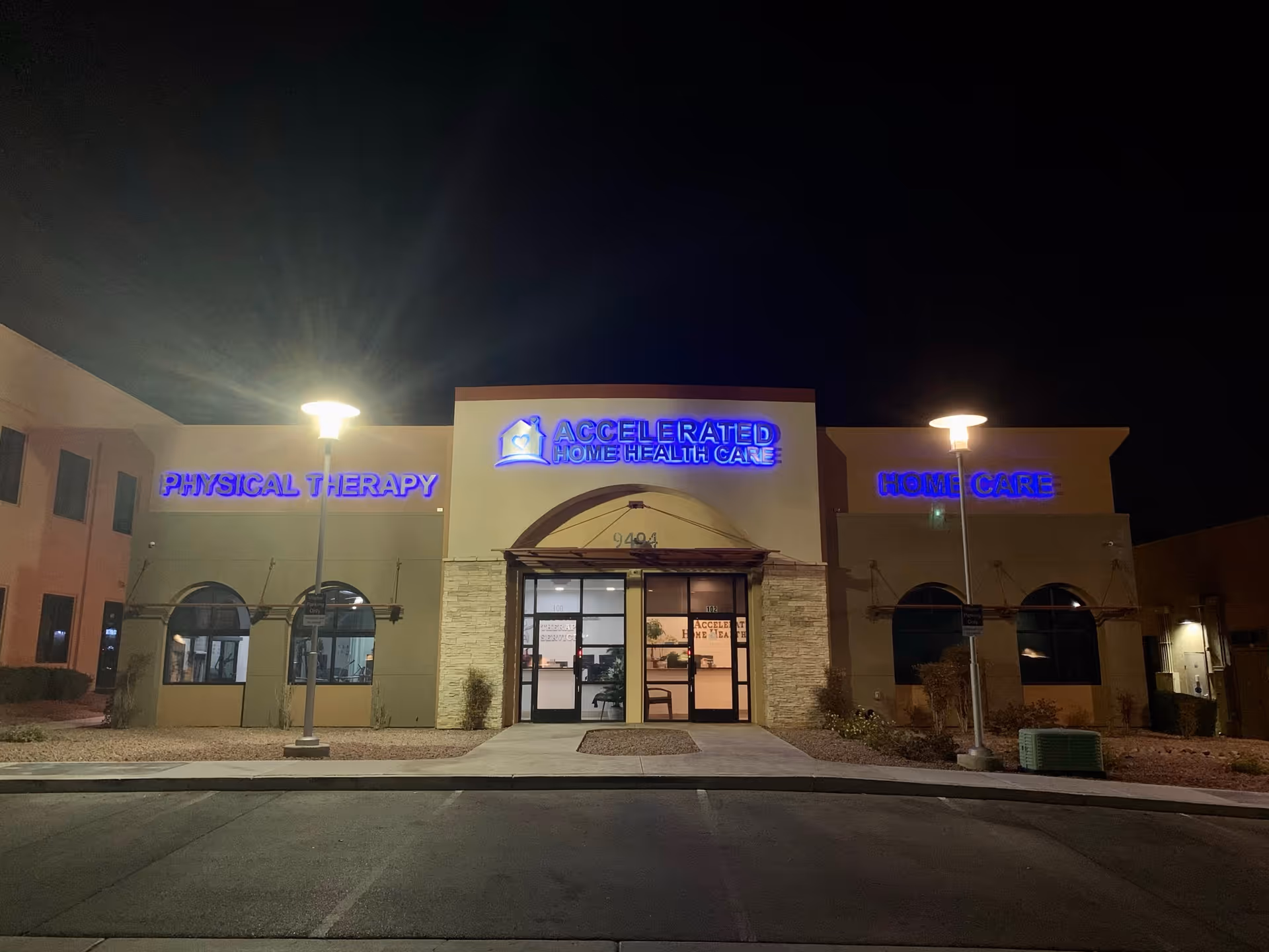 Night exterior of Accelerated Home Health Care facility with blue illuminated signs and entrance.