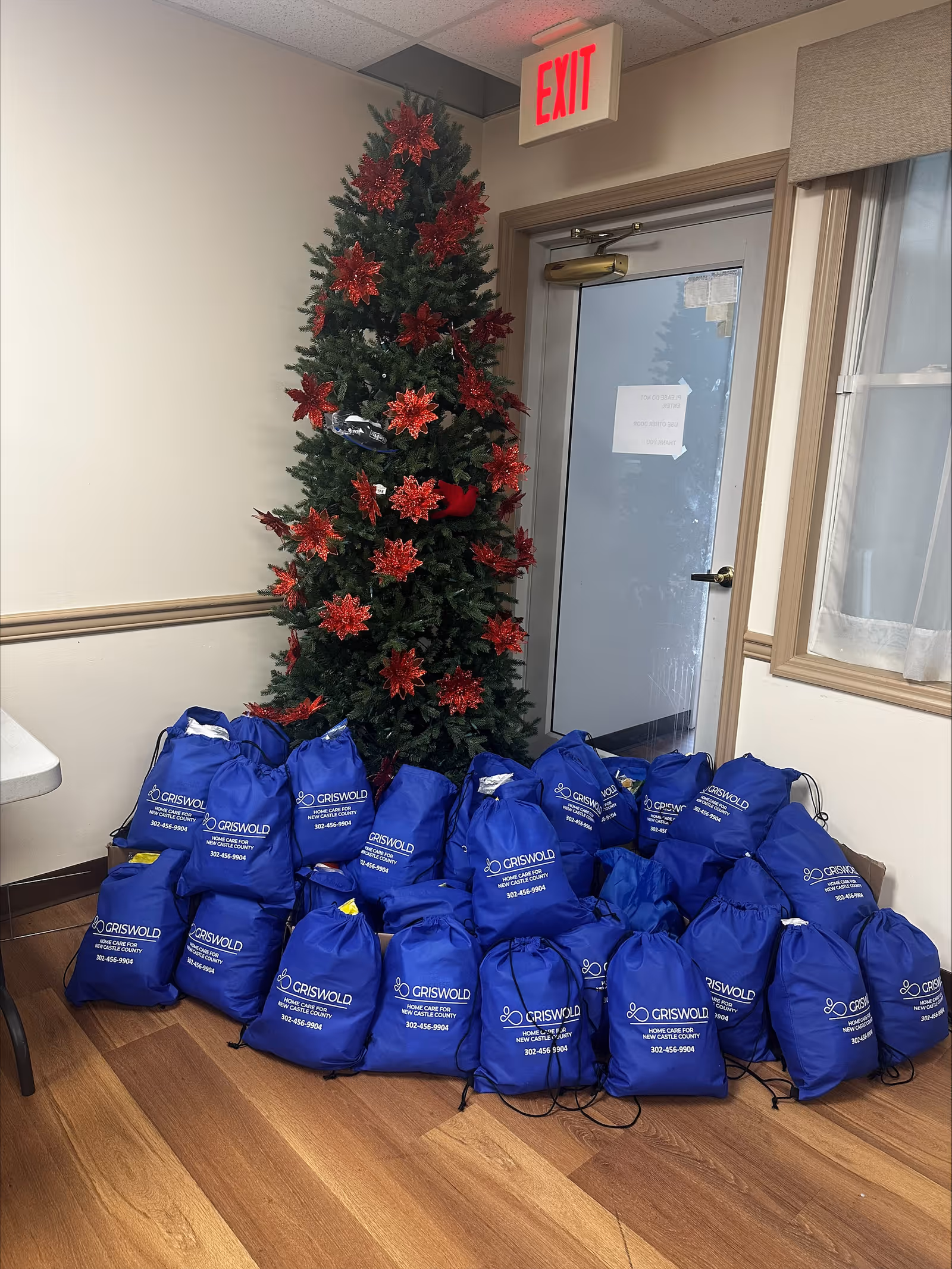 Interior corner with a Christmas tree and blue Griswold bags by an exit door.