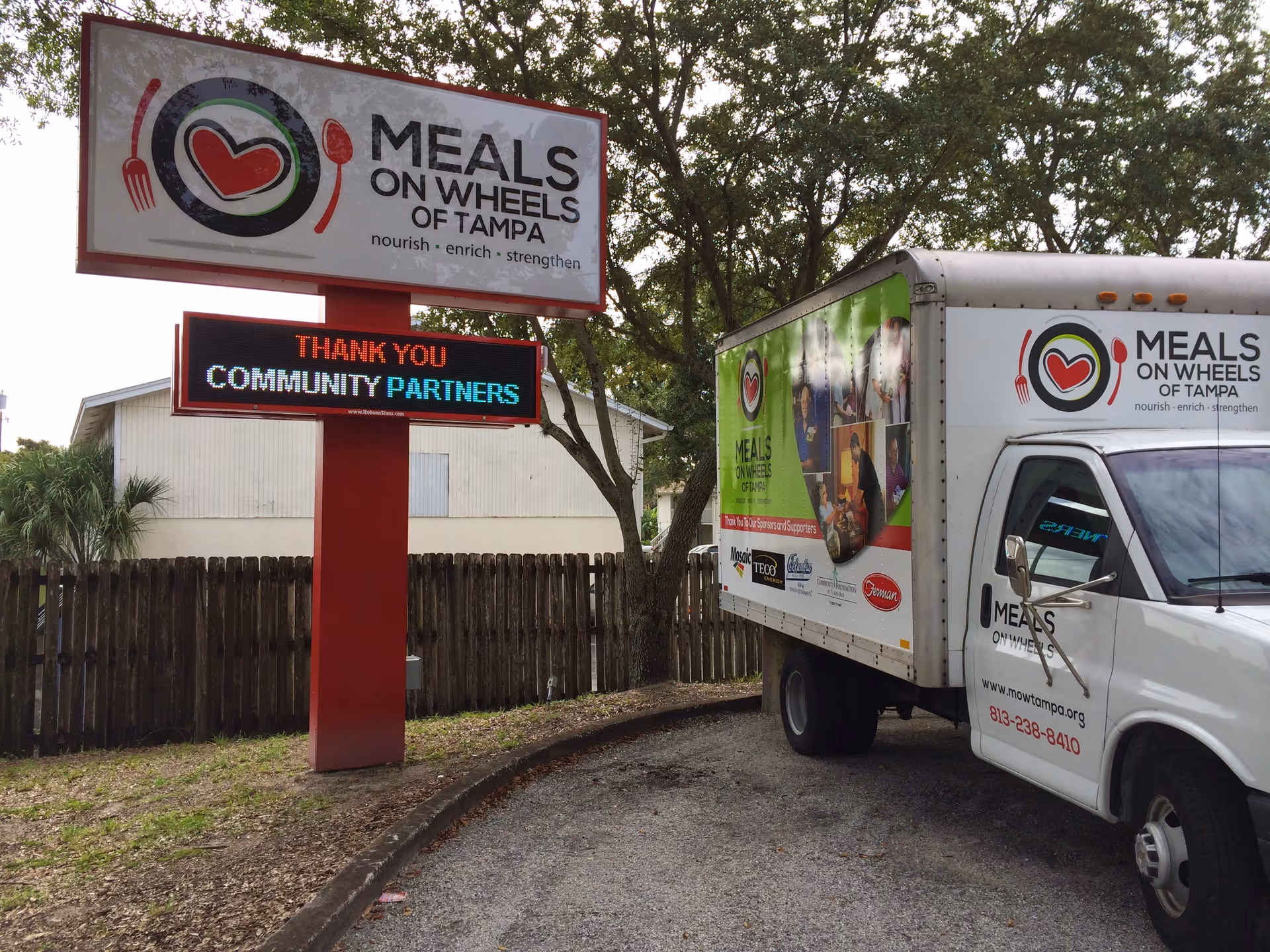 Outdoor scene with Meals On Wheels of Tampa sign and delivery truck.
