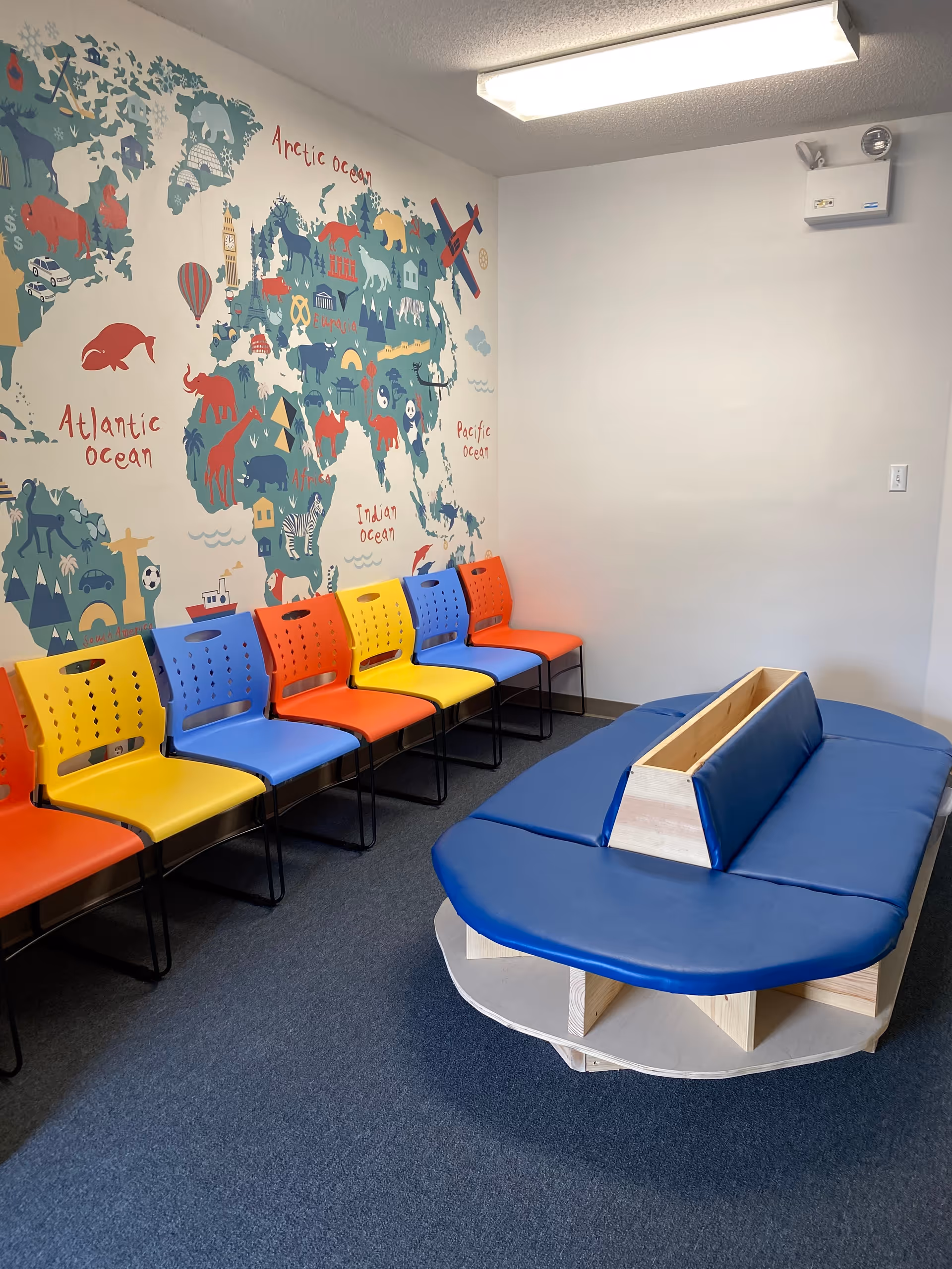 Colorful chairs along a wall mural of a world map in a bright activity room.