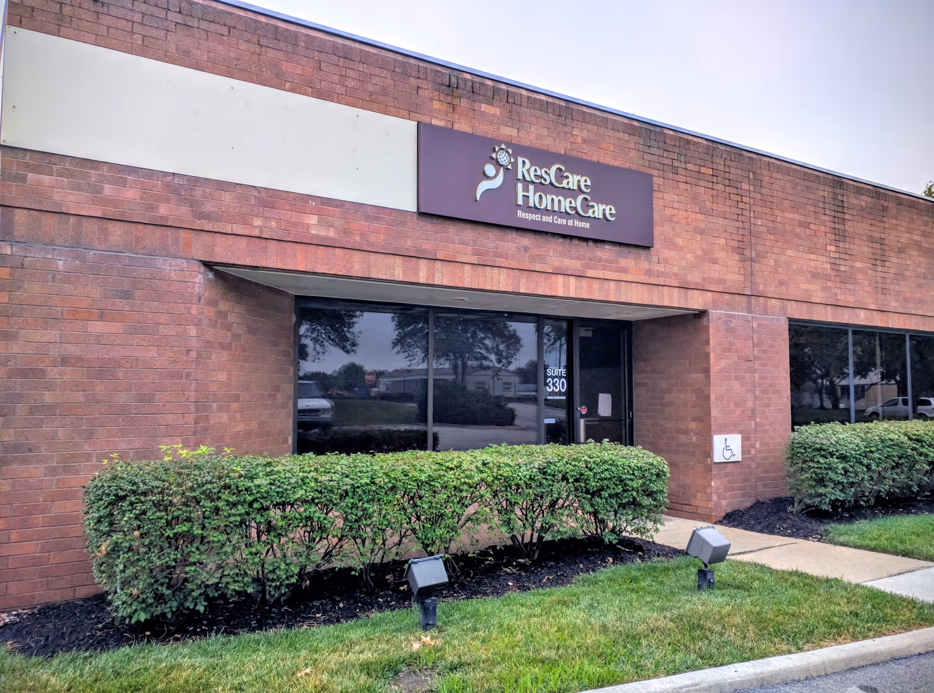 Brick exterior of ResCare HomeCare with entrance, hedges, and a handicap sign.