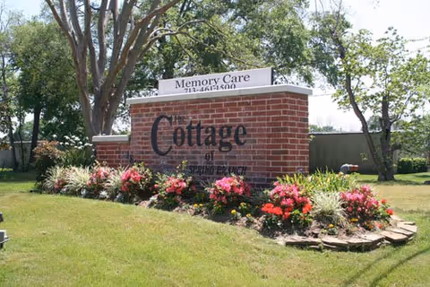 Brick sign for Cottage of Spring Branch with colorful flower beds and trees.