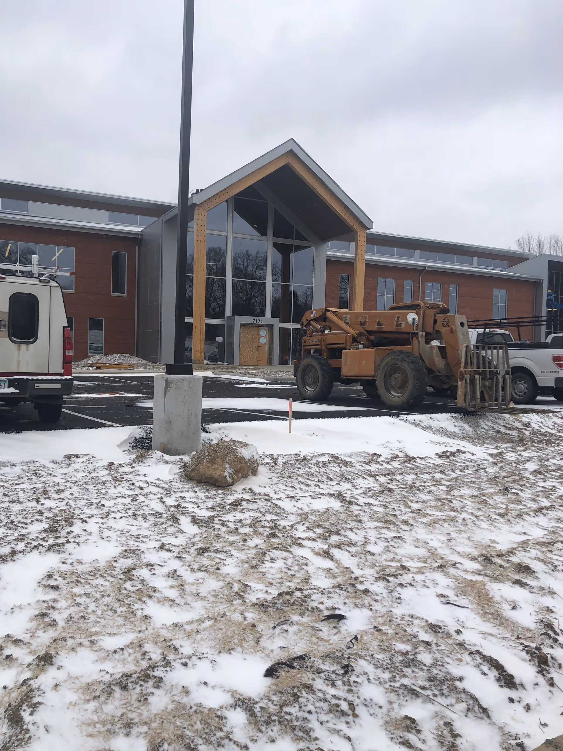 Front view of a modern facility entrance with a wooden canopy and construction equipment outside.