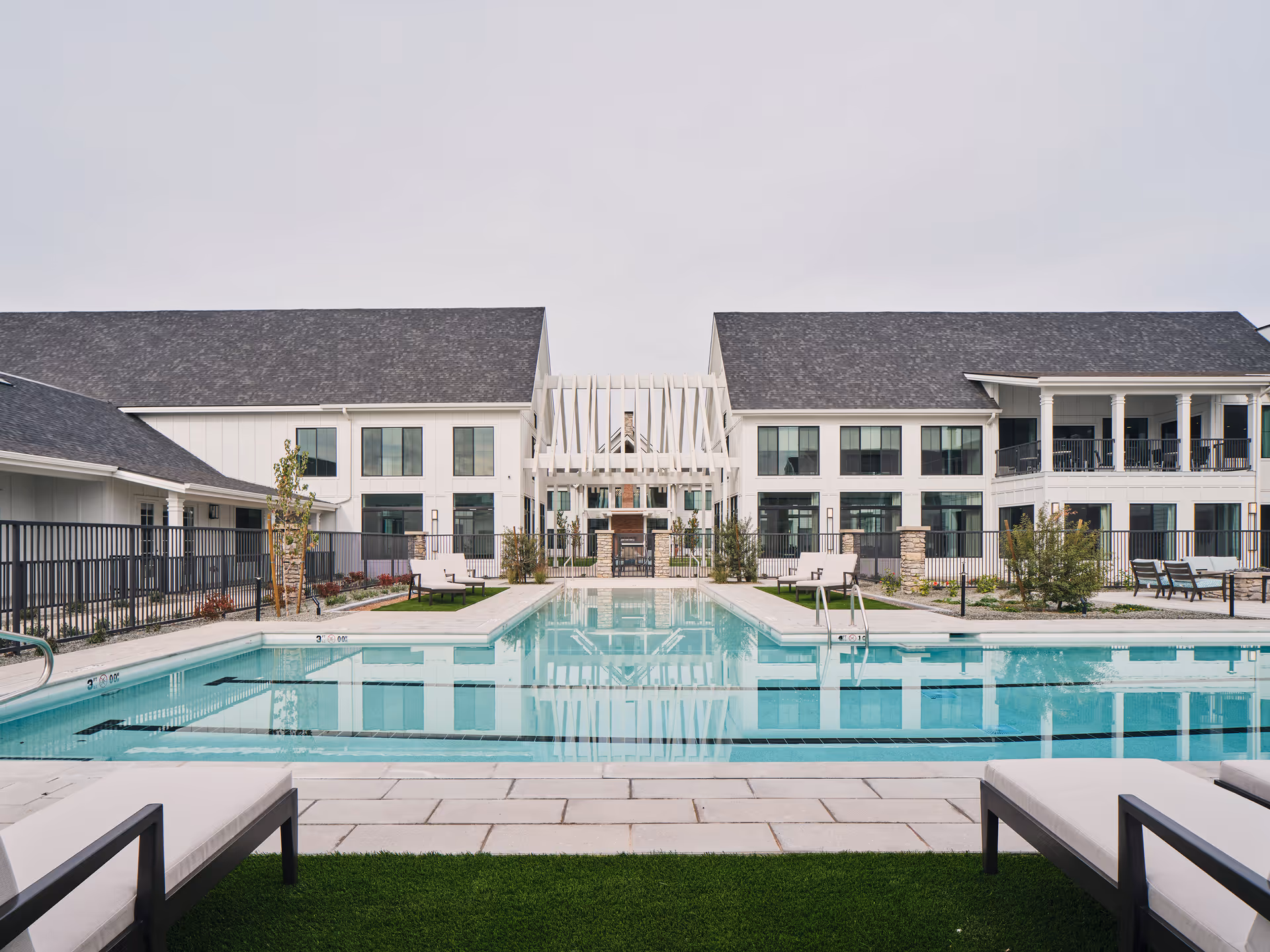 Outdoor view of a senior living facility's pool area with lounge chairs and a two-story white building in the background.