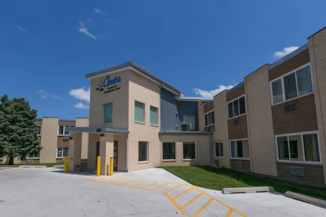 Front entrance of a low-rise brick nursing and rehabilitation center under a blue sky.