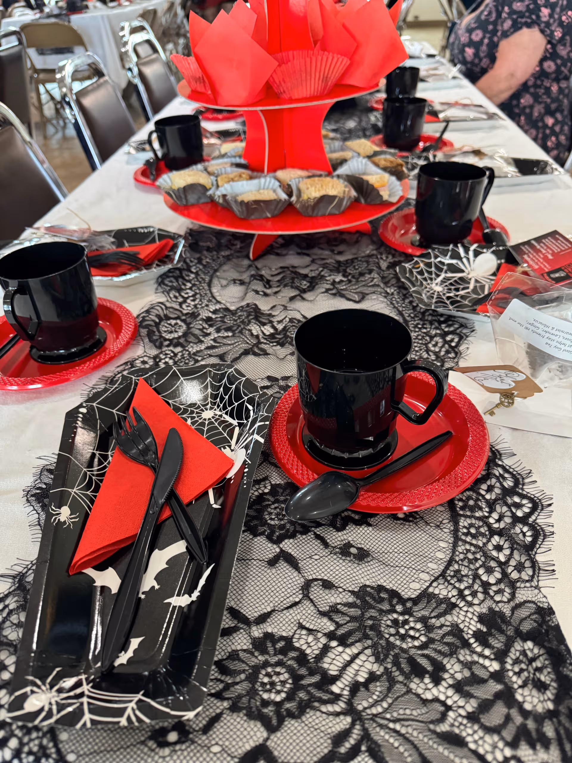Halloween-themed table setting with black lace runner, red napkins, and black dishware.