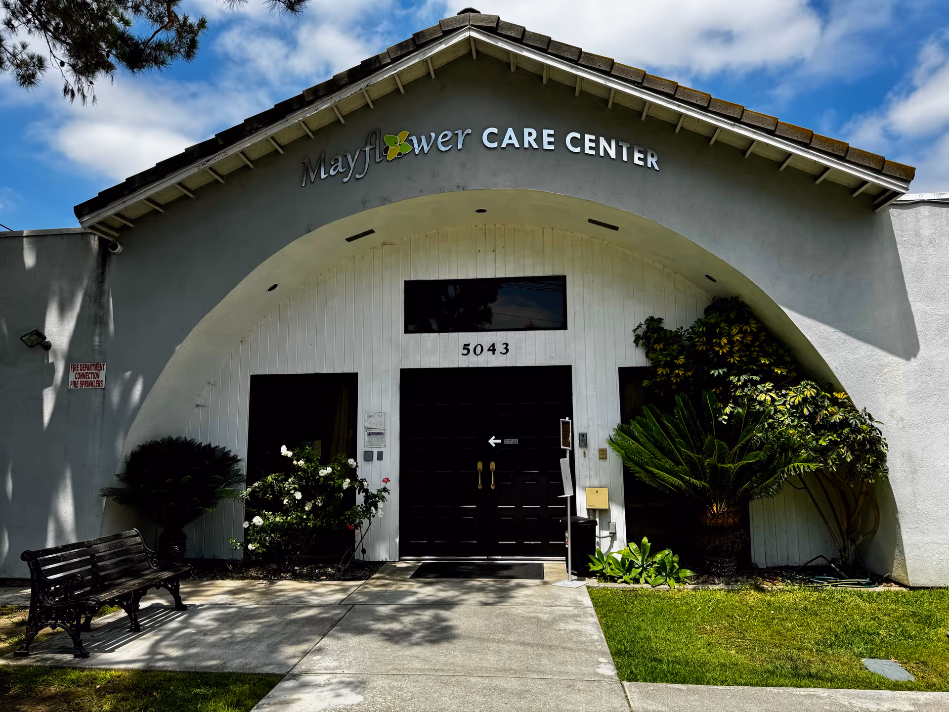 Front view of Mayflower Care Center entrance with arched doorway and greenery.