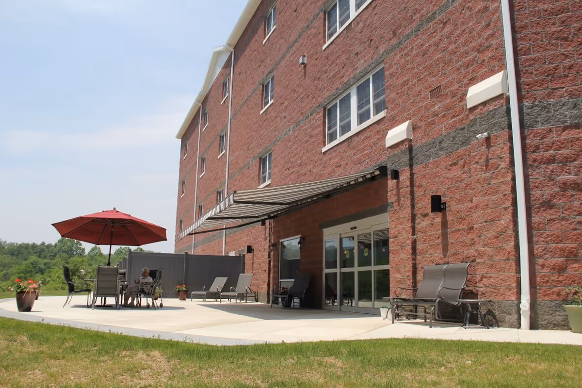 Patio with chairs, tables and a red umbrella next to the brick exterior and entrance of a senior living building.